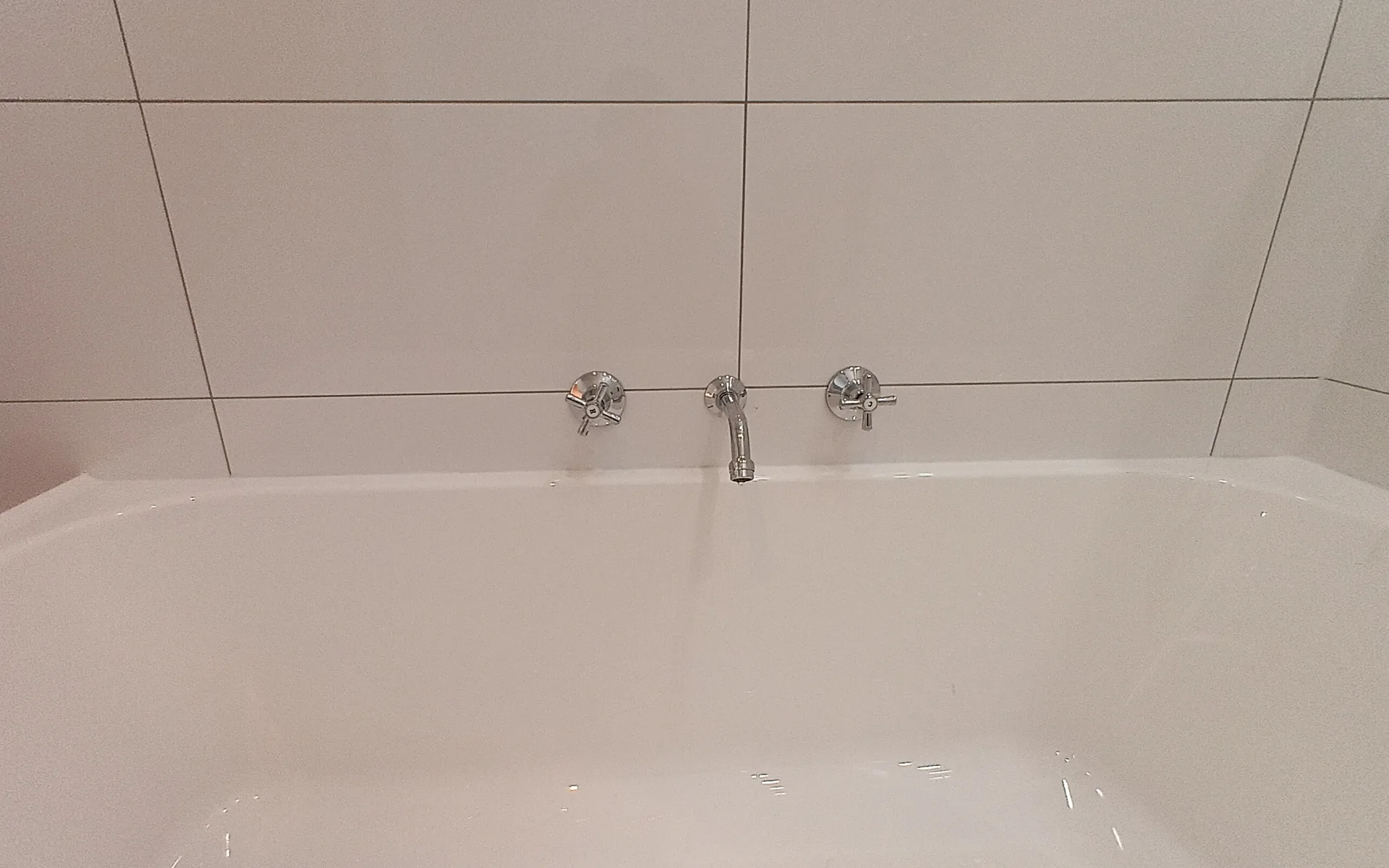 New wall mixer set and bath spout fitted above a white bath