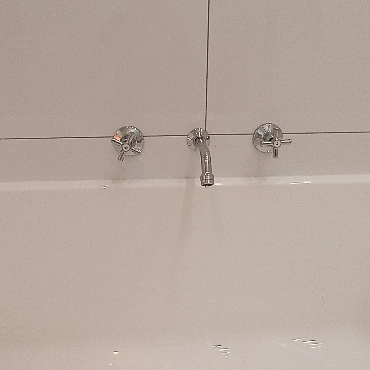New wall mixer set and bath spout fitted above a white bath