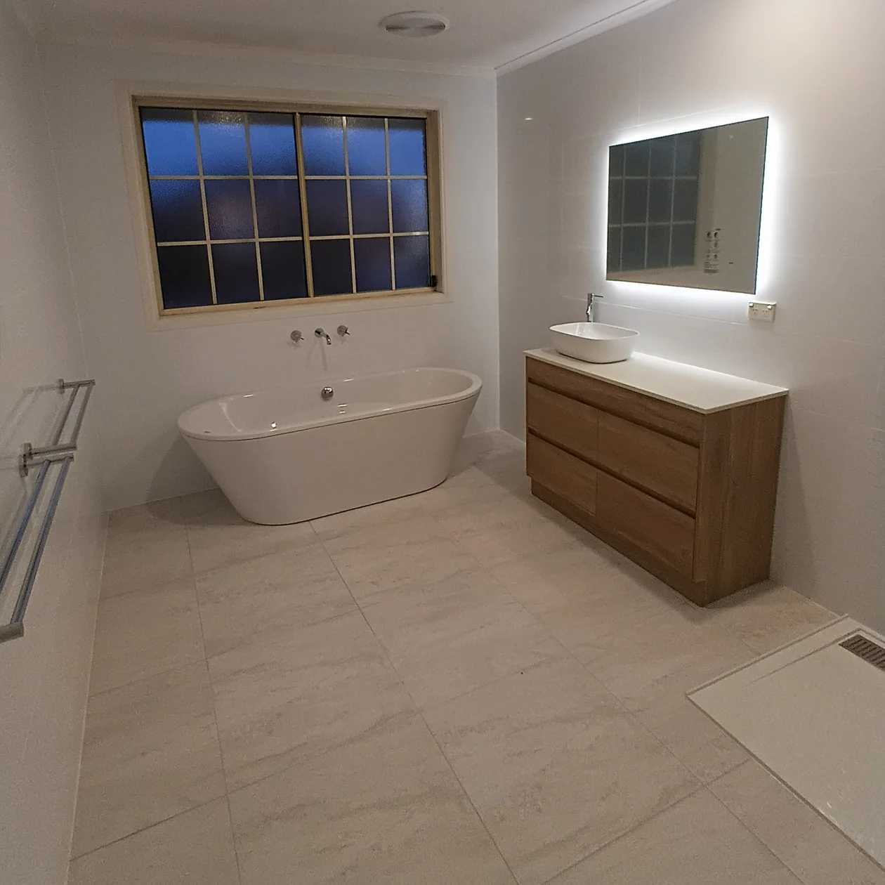 Finished bathroom with a freestanding bath, timber vanity and backlit mirror