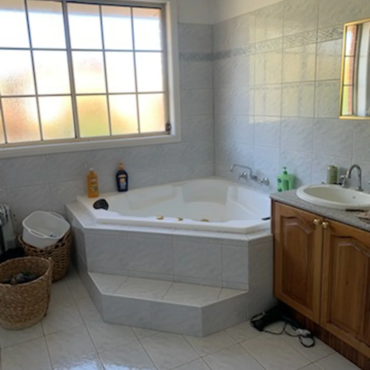Dated bathroom with a corner spa bath and original tiling before renovation