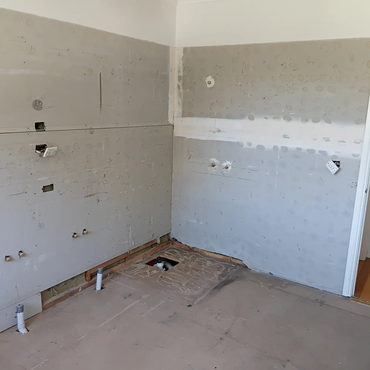 Wall stripped back showing capped drainage and water pipework