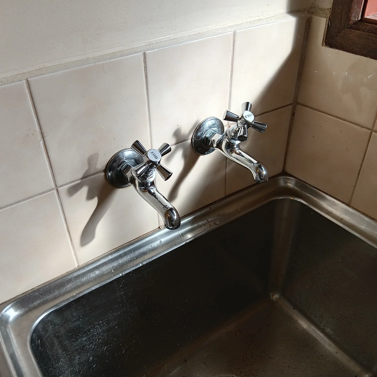 Worn cross handle taps above a stainless steel laundry trough