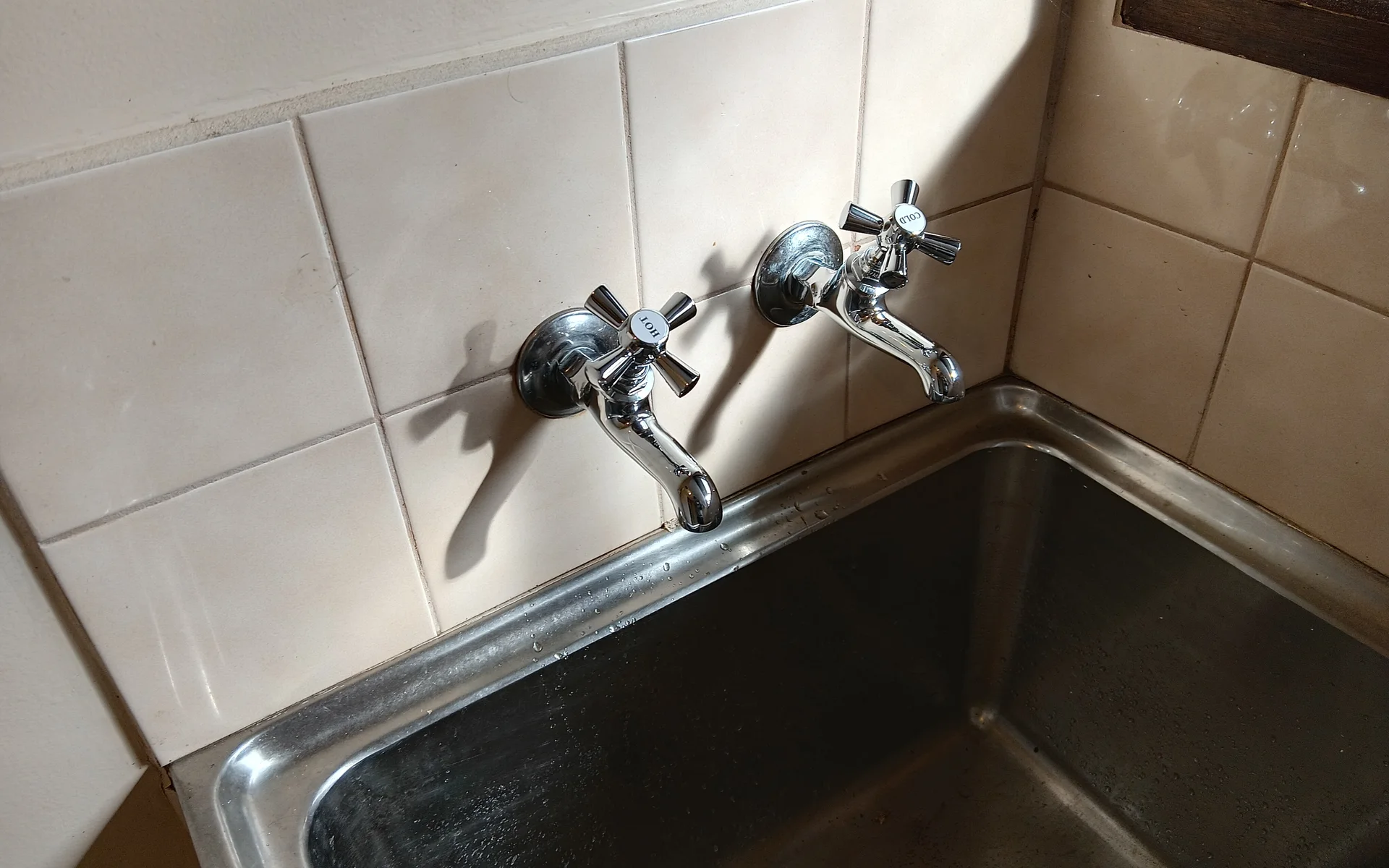 Worn cross handle taps above a stainless steel laundry trough