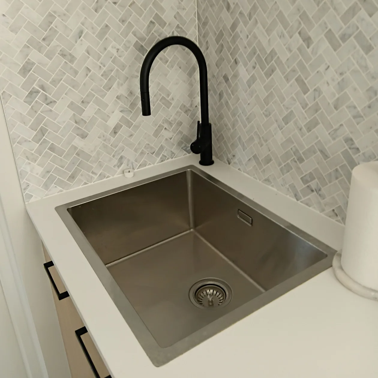 Stainless steel inset sink with a matte black pull-out mixer and marble herringbone splashback