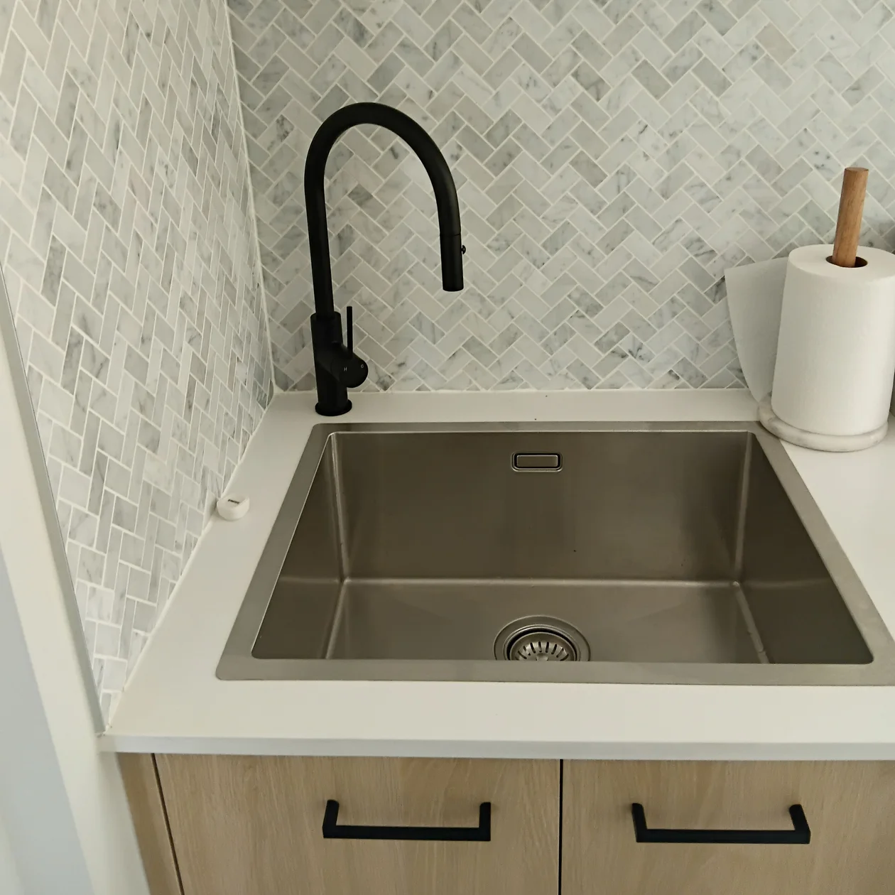 Matte black pull-out mixer fitted off above a stainless steel sink with a marble herringbone splashback